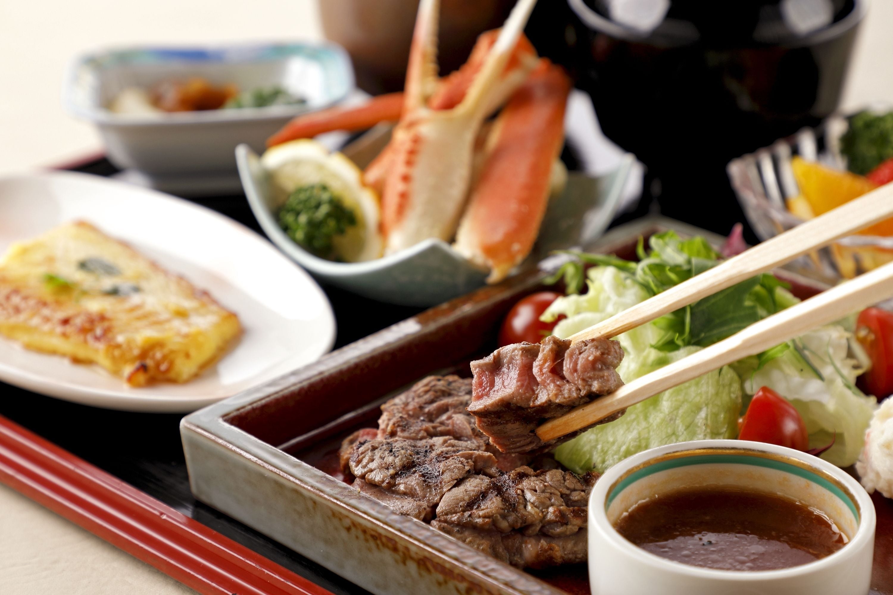 A tray with grilled meat, a bowl of soup, and a plate of vegetables.