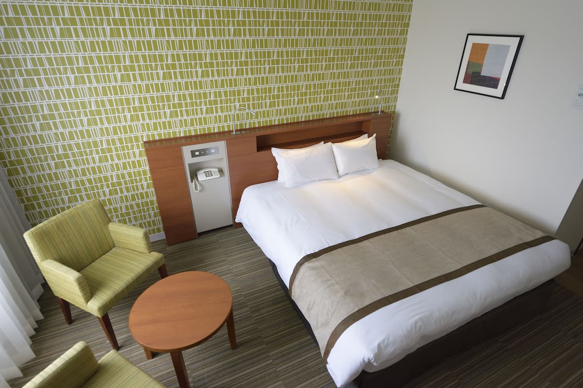 A hotel room with a bed, a desk, a chair, and a small table.