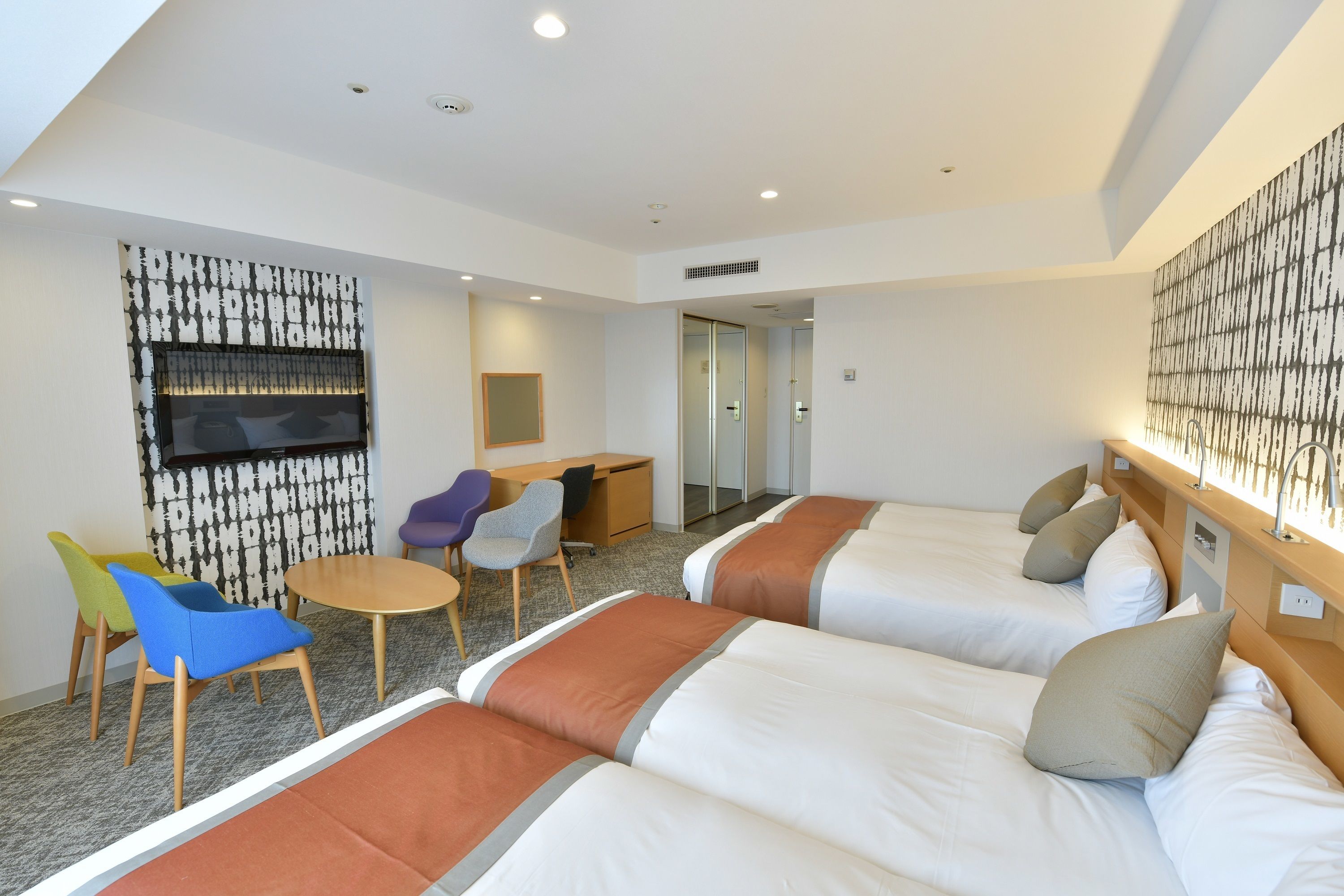 Habitación de hotel con tres camas, un escritorio y una zona de estar con sillas.