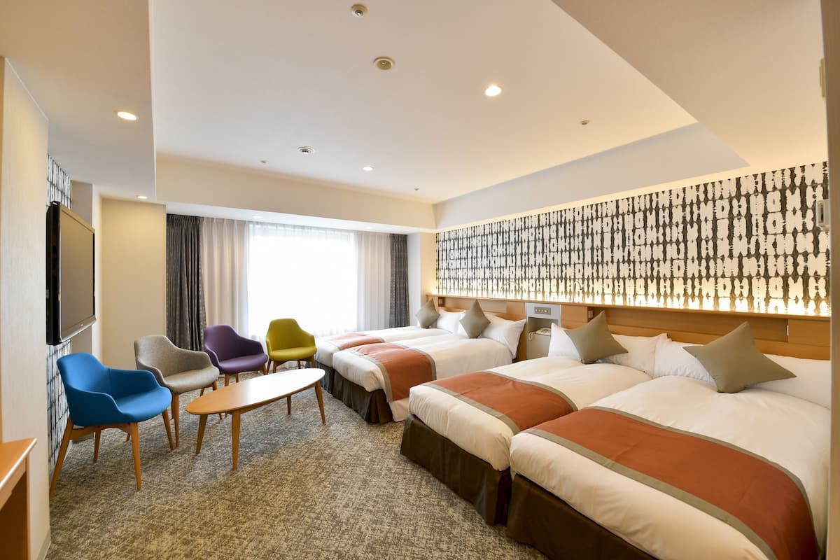 A hotel room with two beds, a TV, a small table, and colorful chairs.