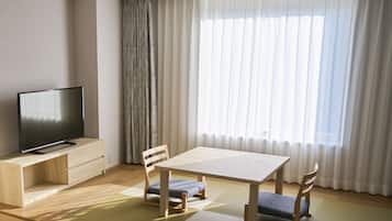 Un salon moderne avec un téléviseur à écran plat posé sur un meuble en bois, une table à manger en bois avec deux chaises, et une grande fenêtre ornée de rideaux légers.