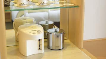 Una zona de cocina con cafetera, cocedor de arroz y repisa de vidrio que exhibe objetos de cerámica blanca.