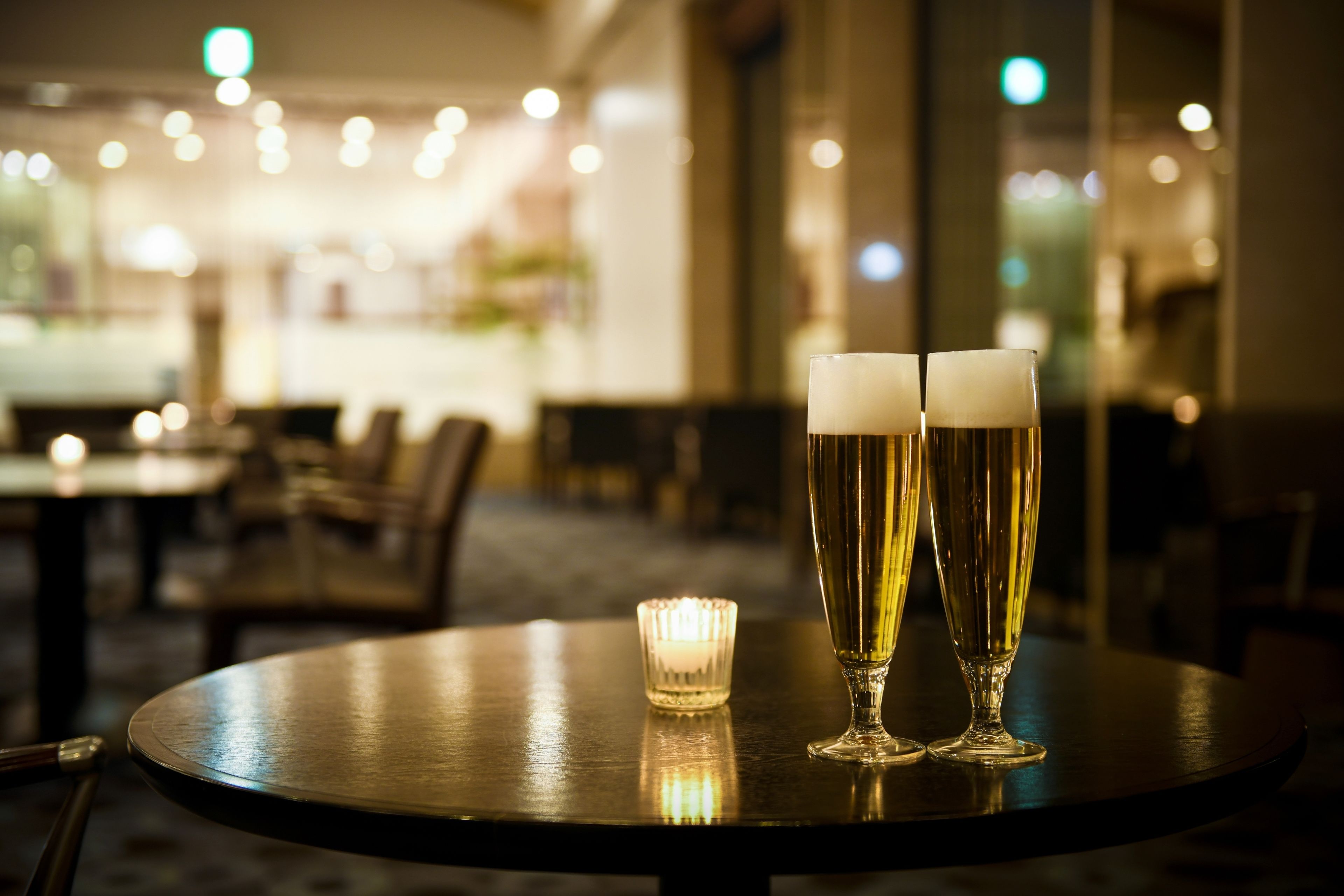 Two glasses of beer on a round table with a lit candle in the center.