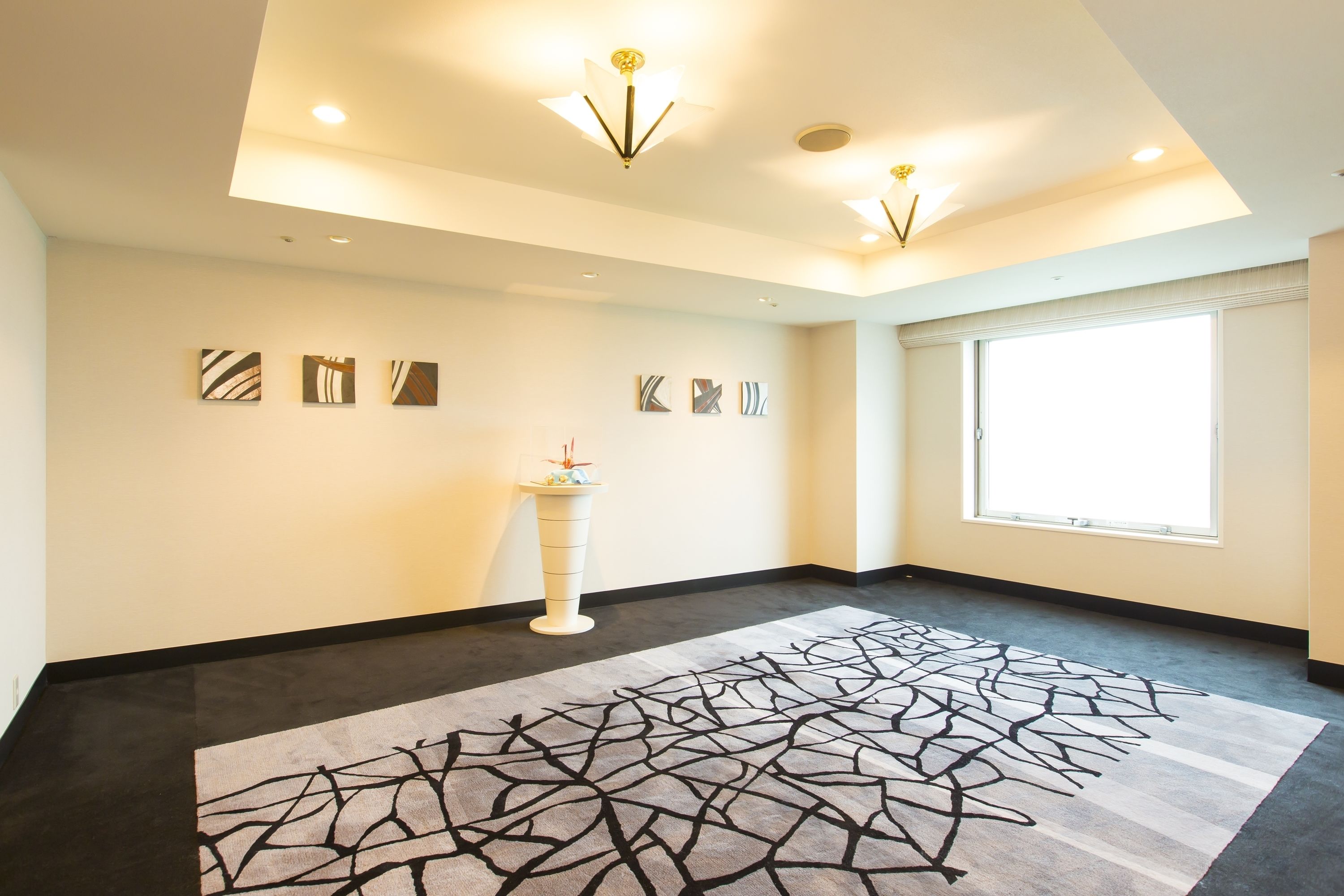 Quarto de hotel com uma janela grande, design moderno no teto e tapete estampado.