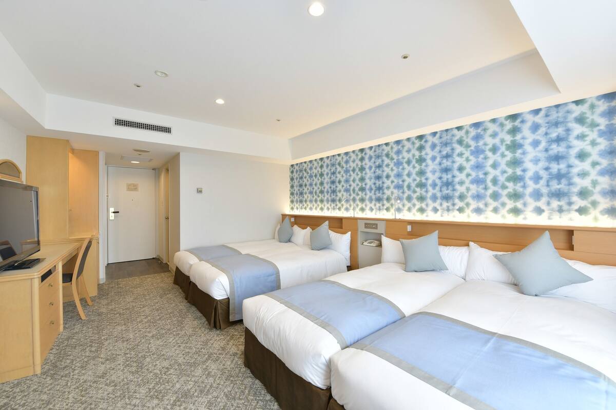 A hotel room with three beds, a desk, and a TV.