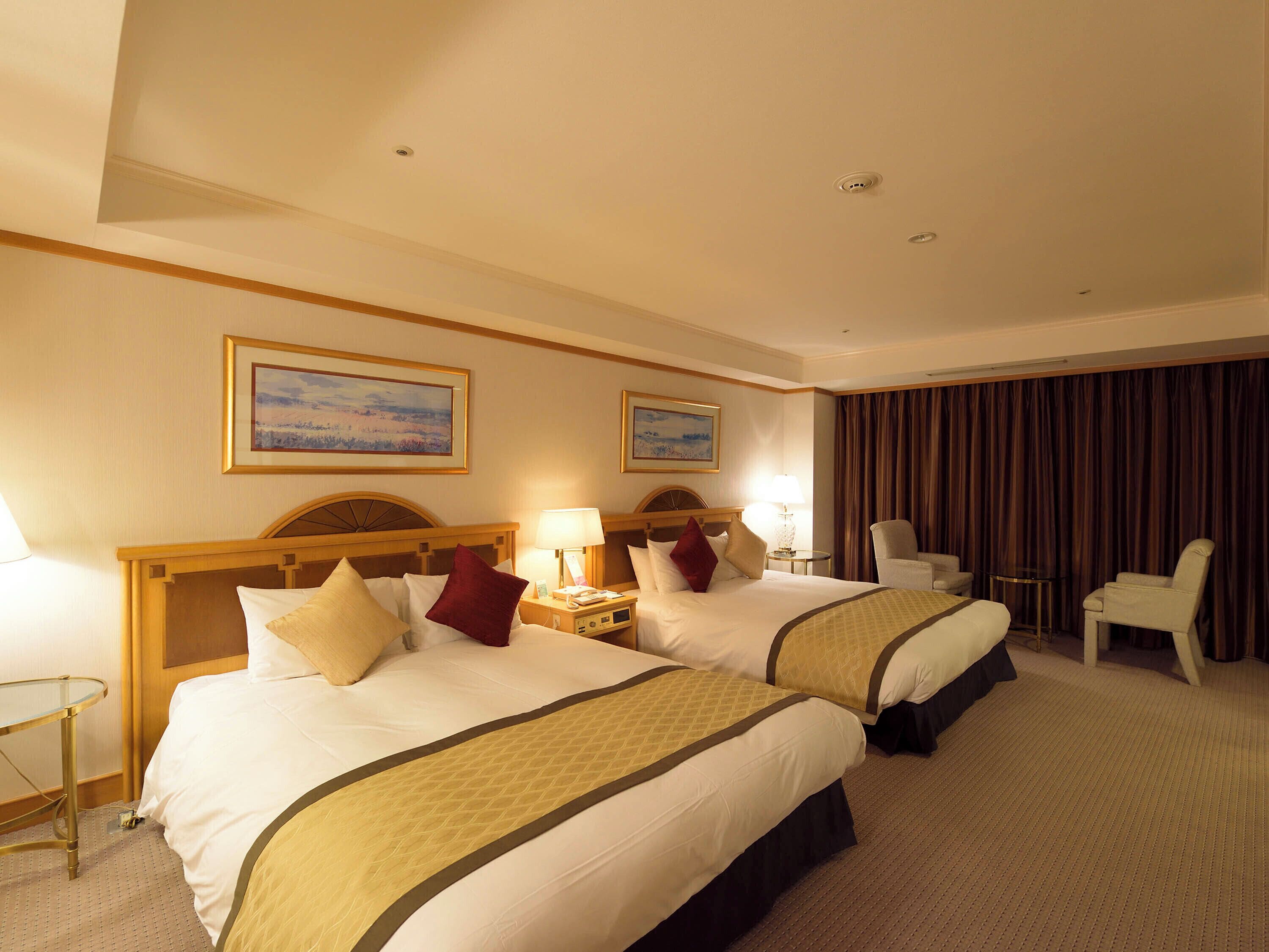 A hotel room with two beds, a desk, and a chair.