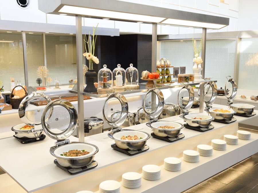 A buffet setup with multiple food stations, clear glass covers, and neatly stacked plates.