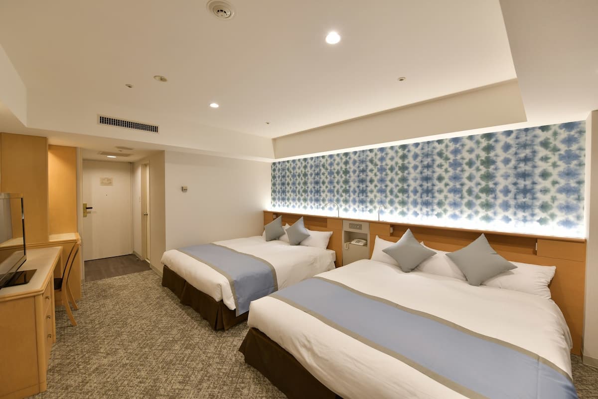 A hotel room with two beds, a desk, and a television.