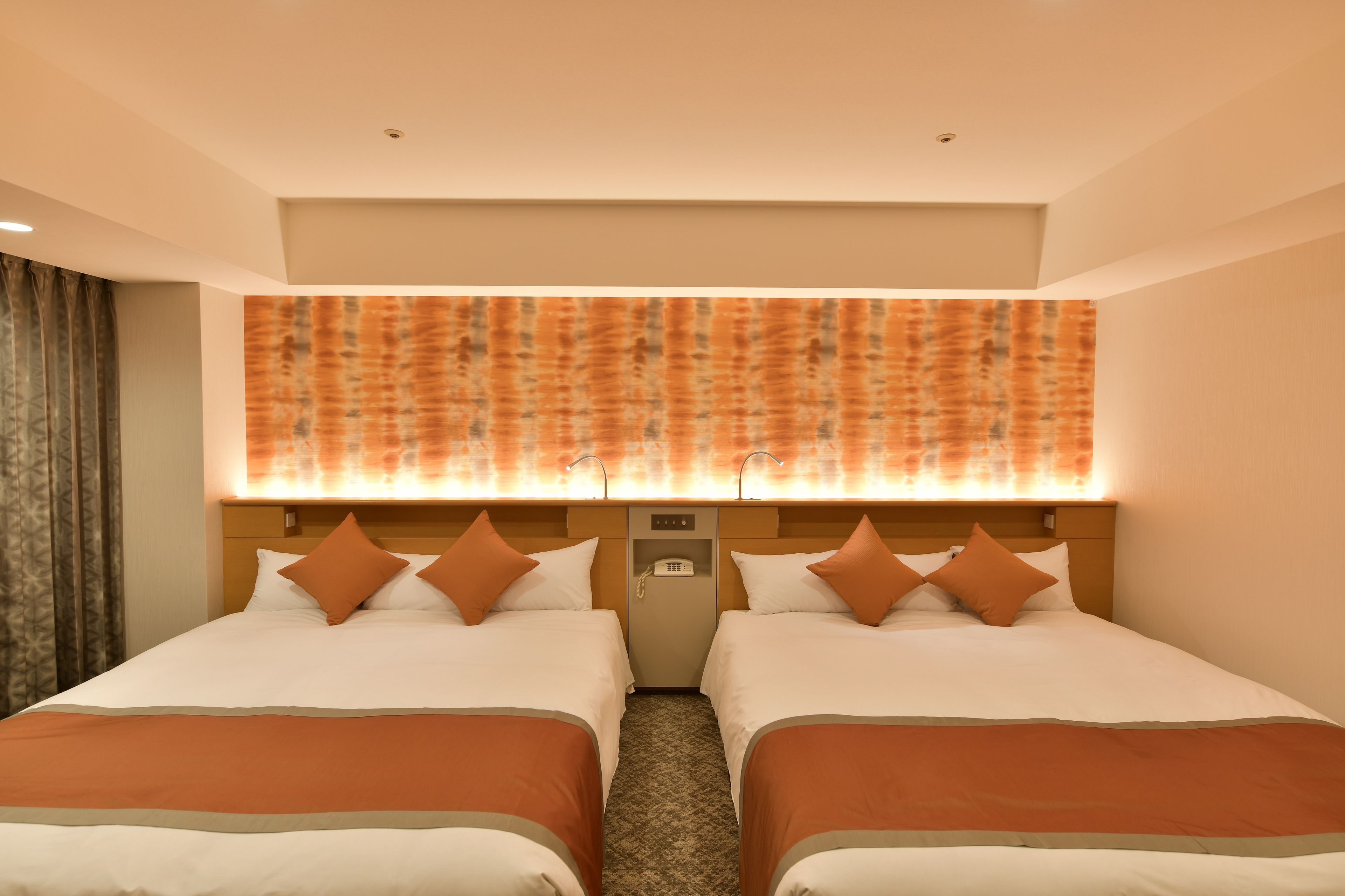 Habitación de hotel con dos camas, cabecero con teléfono y pared decorada sobre las camas.