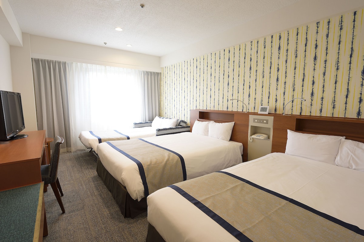 A hotel room with two beds, a desk, a chair, a television, and a window with curtains.