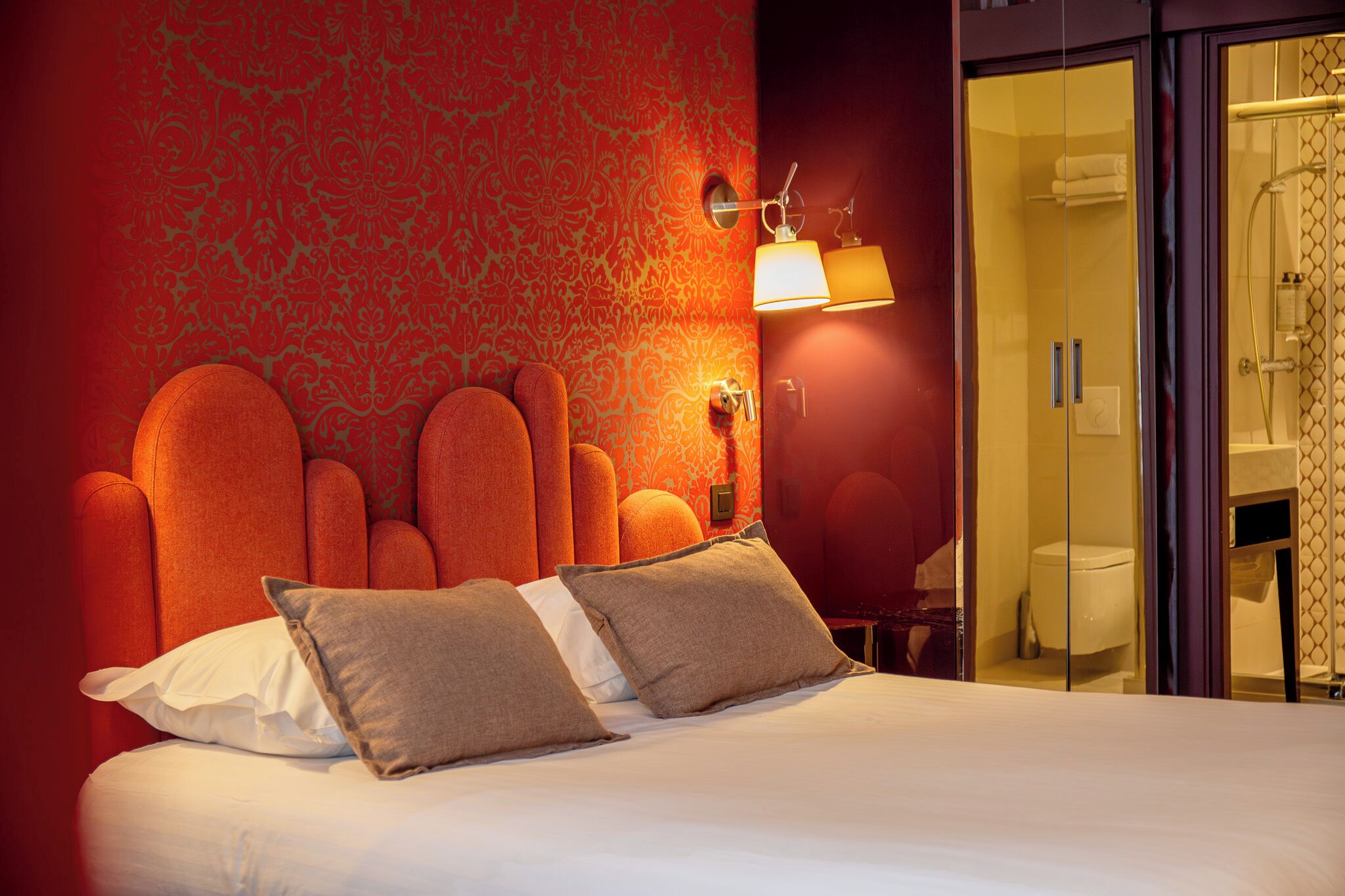 Een hotelkamer met een groot bed, een wandlamp en een glazen deur naar een badkamer.
