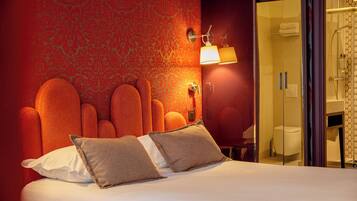 Ein Hotelzimmer mit einem großen Bett, einer Wandlampe und einer Glastür zu einem Badezimmer.