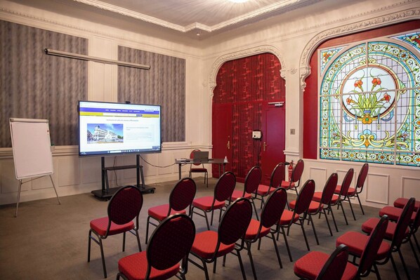A conference room with a whiteboard, a large screen, and red chairs arranged in rows.