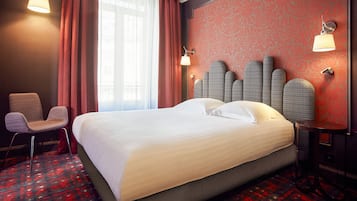 A hotel room with a large bed, a chair, a table, and a wall-mounted lamp.