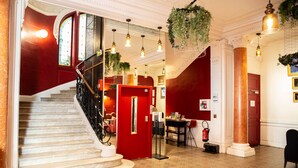 A grand staircase with a red door, a fire extinguisher, and hanging plants. - Grand Hôtel du Midi Montpellier - Opéra Comédie (Montpellier)