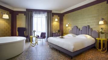 Ein Hotelzimmer mit einem großen Bett, einer Badewanne, einem Sessel, einem kleinen Tisch und einem Spiegel.