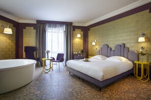 A hotel room with a large bed, a bathtub, a chair, a small table, and a mirror. - Grand Hôtel du Midi Montpellier - Opéra Comédie (Montpellier)
