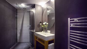 Un baño moderno con ducha envuelta en vidrio, un lavabo blanco con espejo y un perchero para toallas.