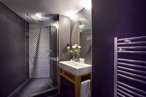 Un baño moderno con ducha envuelta en vidrio, un lavabo blanco con espejo y un perchero para toallas.
