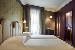 Habitación de hotel con dos camas, una mesita con lámpara, un espejo y una ventana con cortinas.