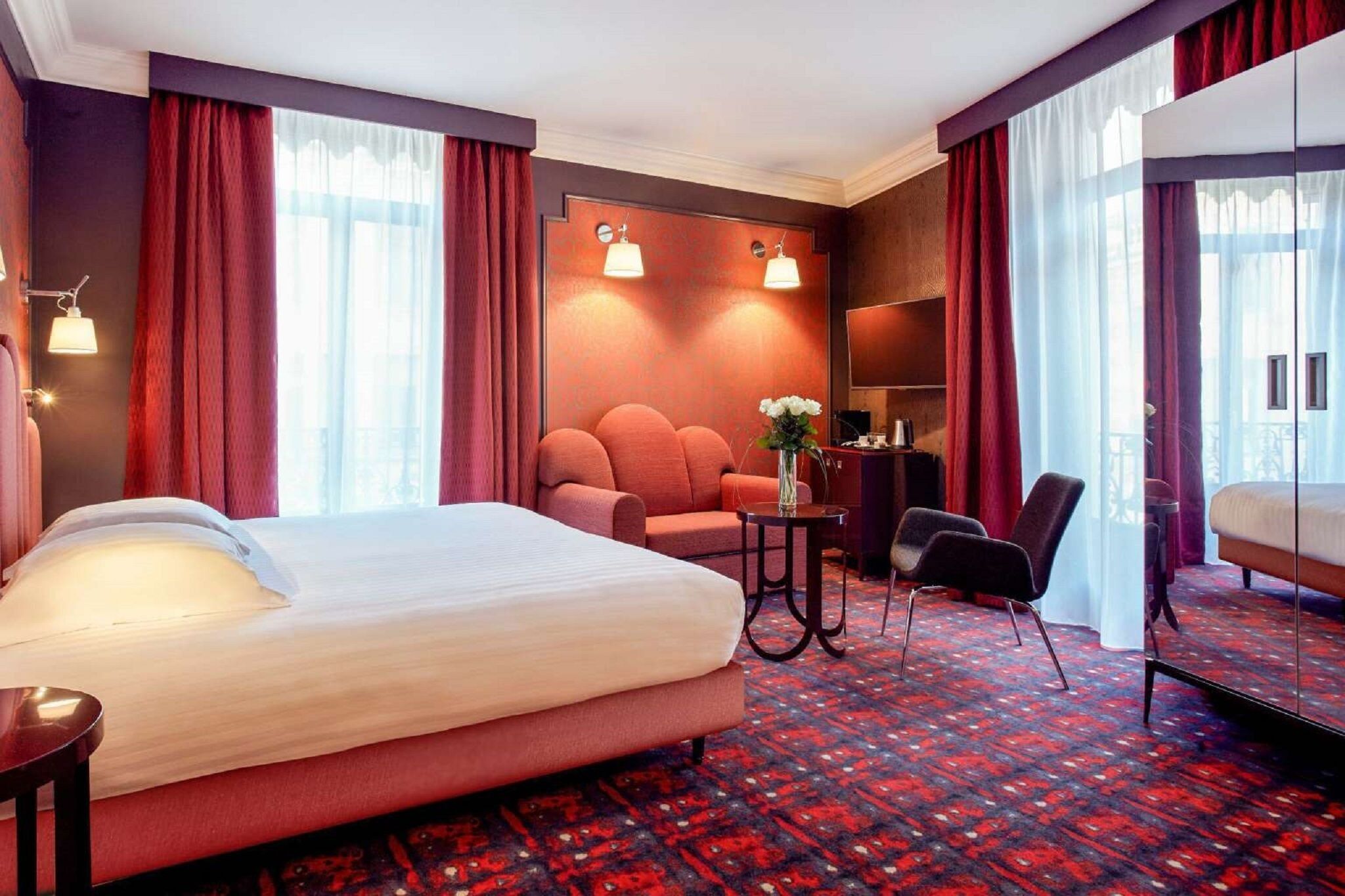 Quarto de hotel com uma cama grande, uma escrivaninha, uma cadeira e uma pequena mesa com um vaso.