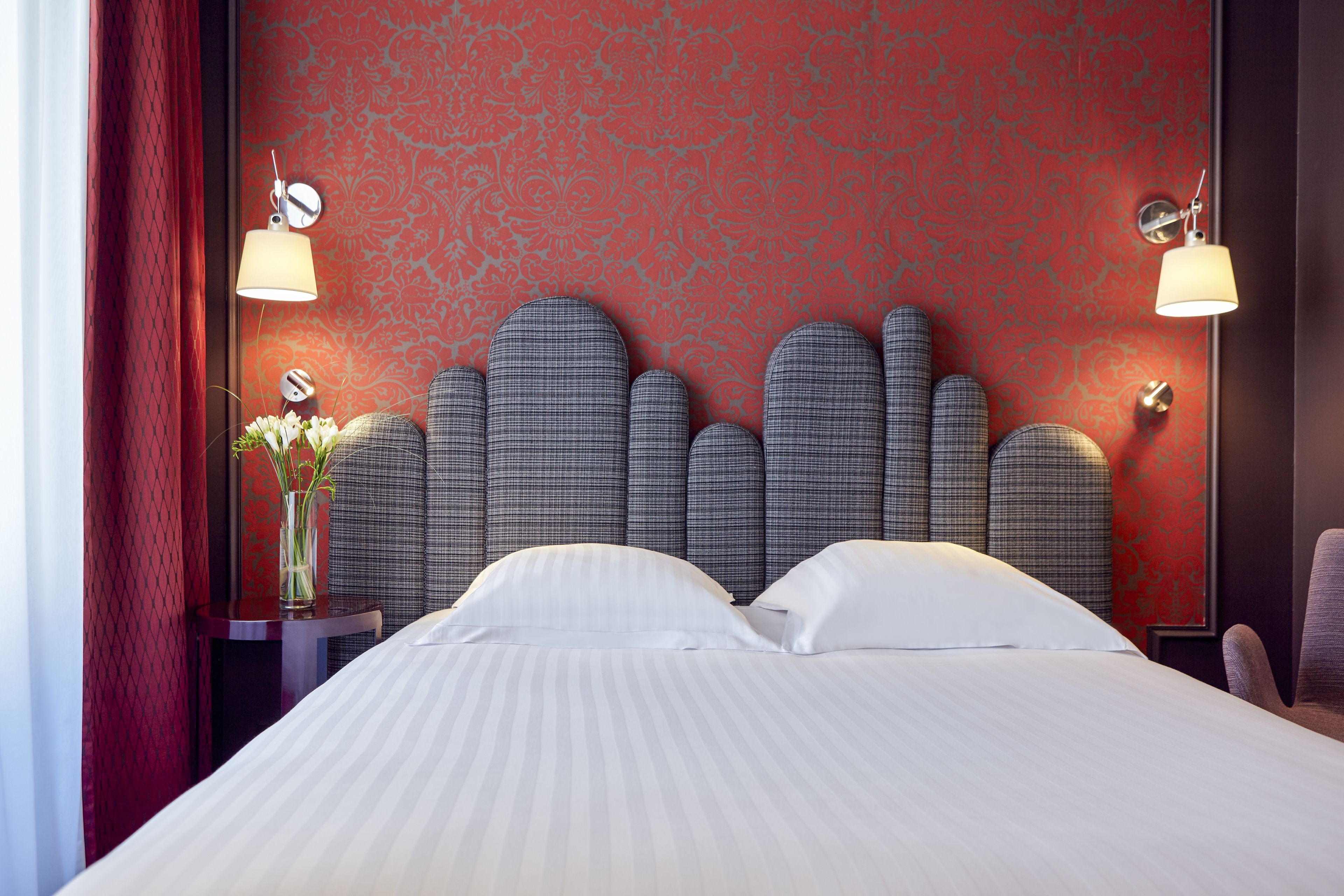 A hotel room with a bed, a nightstand, a lamp, and a vase with flowers.
