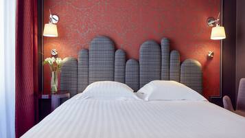 A hotel room with a bed, a nightstand, a lamp, and a vase with flowers.