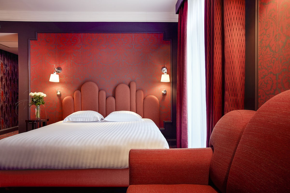 A hotel room with a large bed, two bedside lamps, and a red upholstered chair.