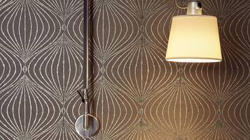 Een kamer met behang met een patroon, een tafel met een lamp en een stoel.