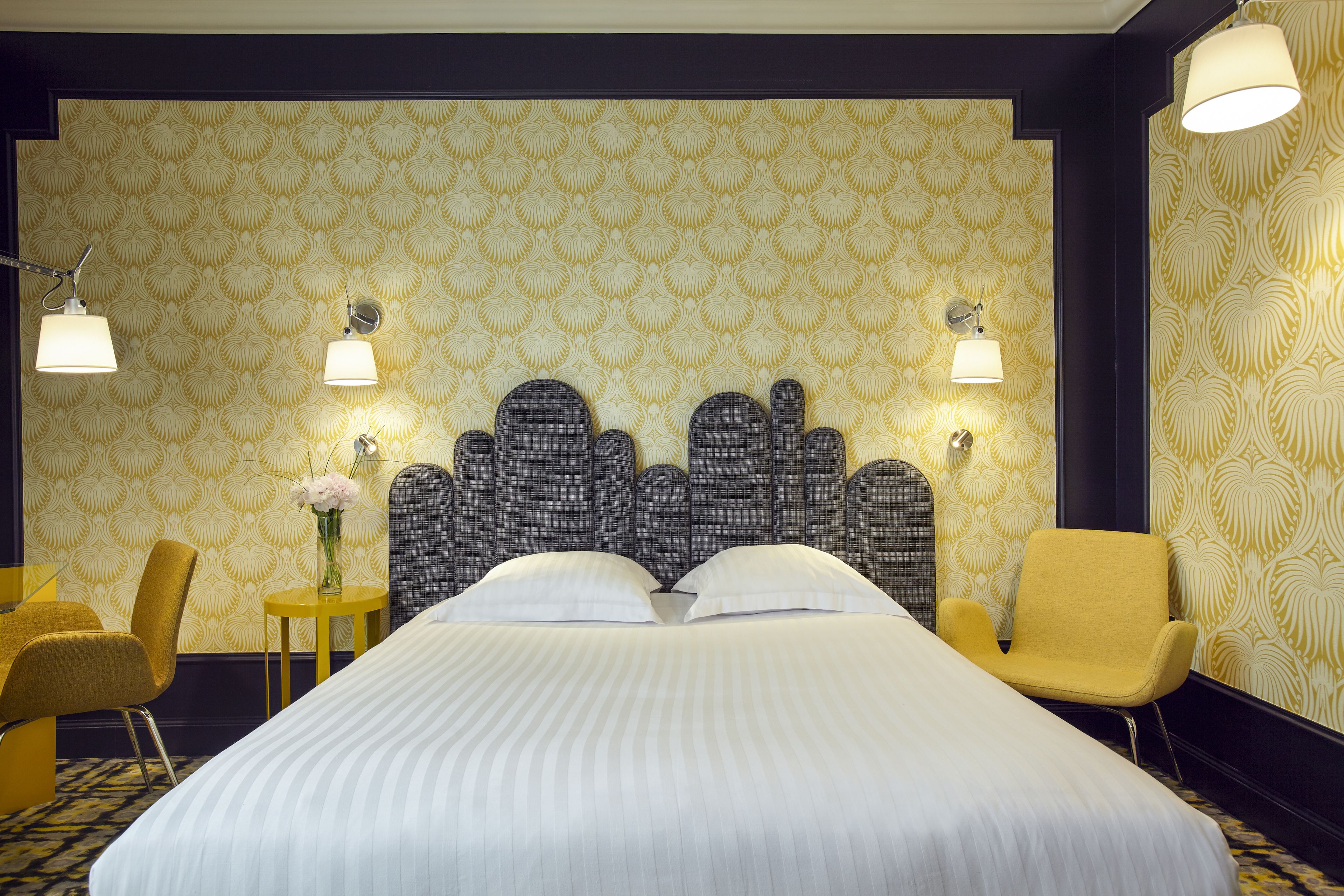 Habitación de hotel con una cama grande, dos lámparas de noche, una mesita con un florero y dos sillas.