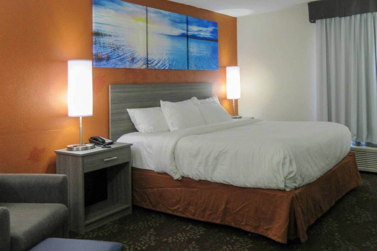A hotel room with a large bed, two bedside lamps, a nightstand, a chair, and a painting on the wall.