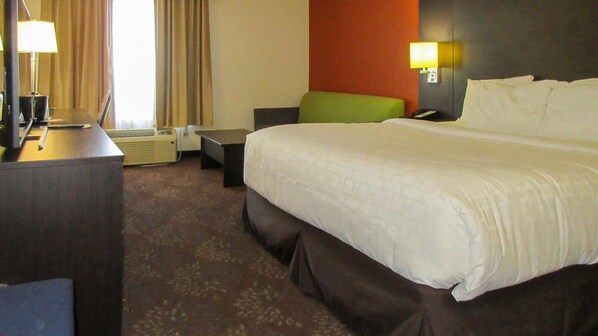 Habitación de hotel con una cama grande, un escritorio con lámpara, una silla y una mesita.