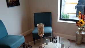 A modern living room with a glass coffee table, a blue armchair, and a vase with flowers. - Clarion Pointe Evansville North (Evansville)