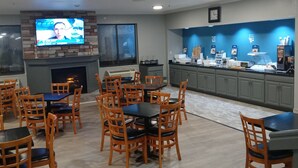 A restaurant with a TV mounted on the wall, wooden tables and chairs, and a counter with food items. - Clarion Pointe Evansville North (Evansville)