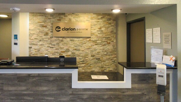 A reception desk with a stone wall backdrop, a sign for Clarion Pointe by Choice Hotels, and a Dell computer on the counter. - Clarion Pointe Evansville North (Evansville)