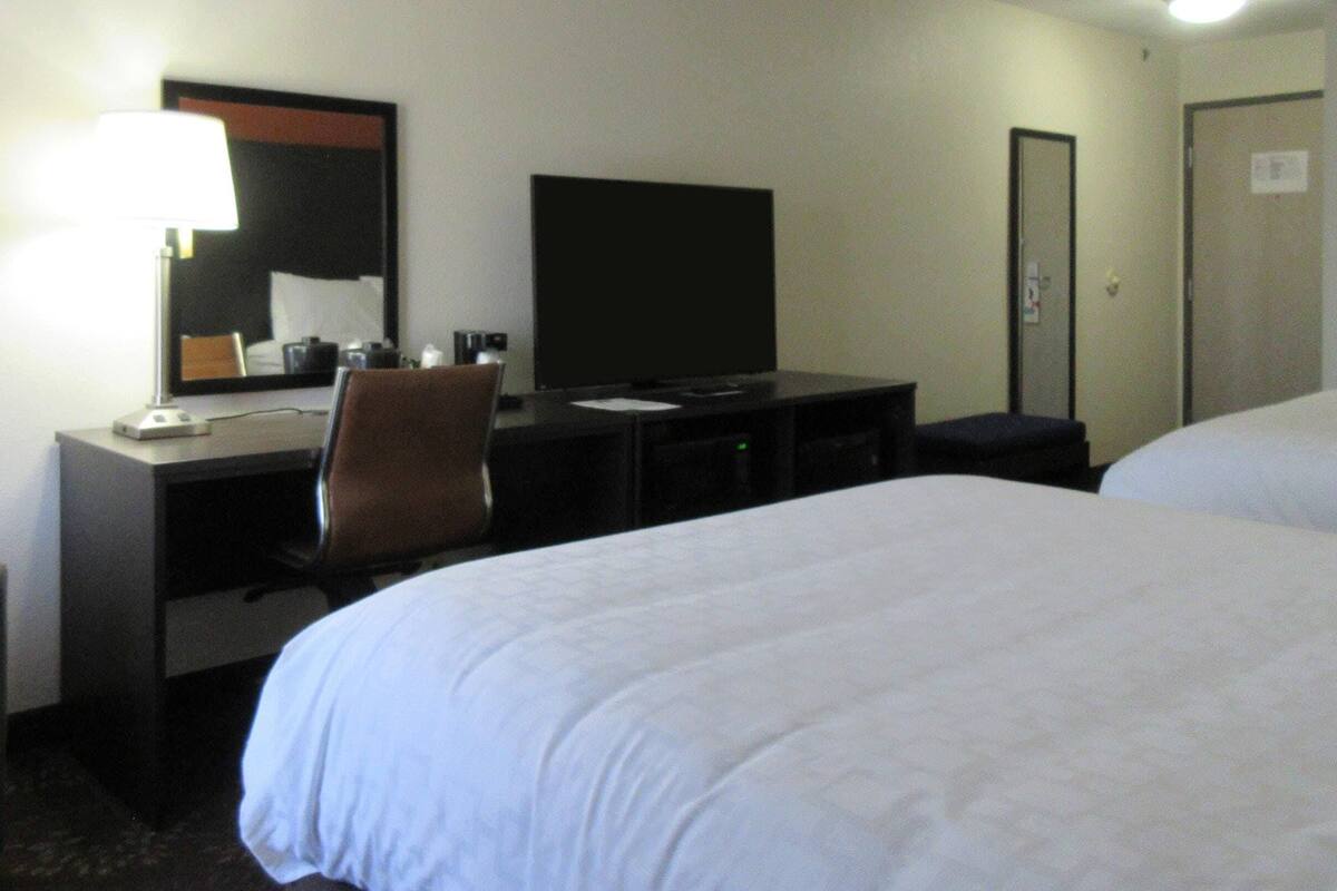 A hotel room with a bed, a desk, a chair, a television, and a door.