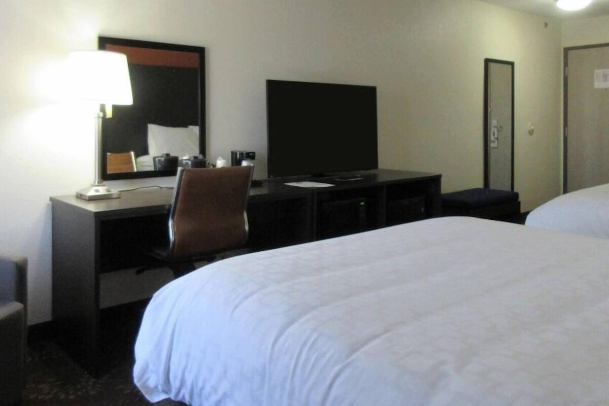 A hotel room with a bed, a desk with a chair, a television, and a mirror.
