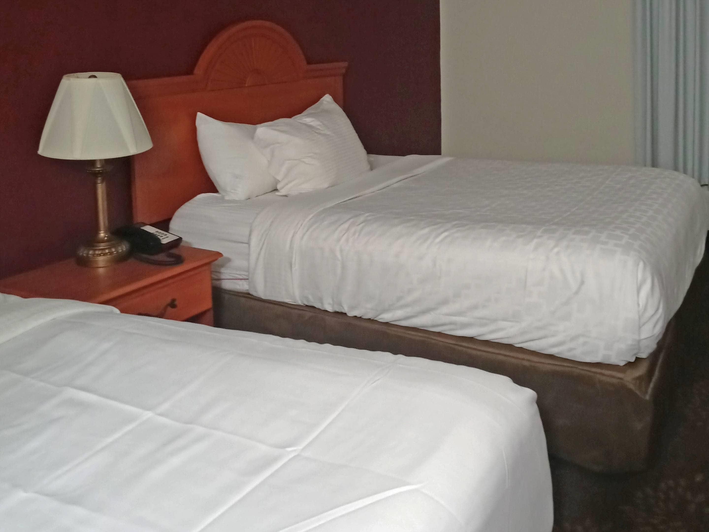 Una habitación de hotel con dos camas, una mesita de noche con lámpara y un cabecero de madera.