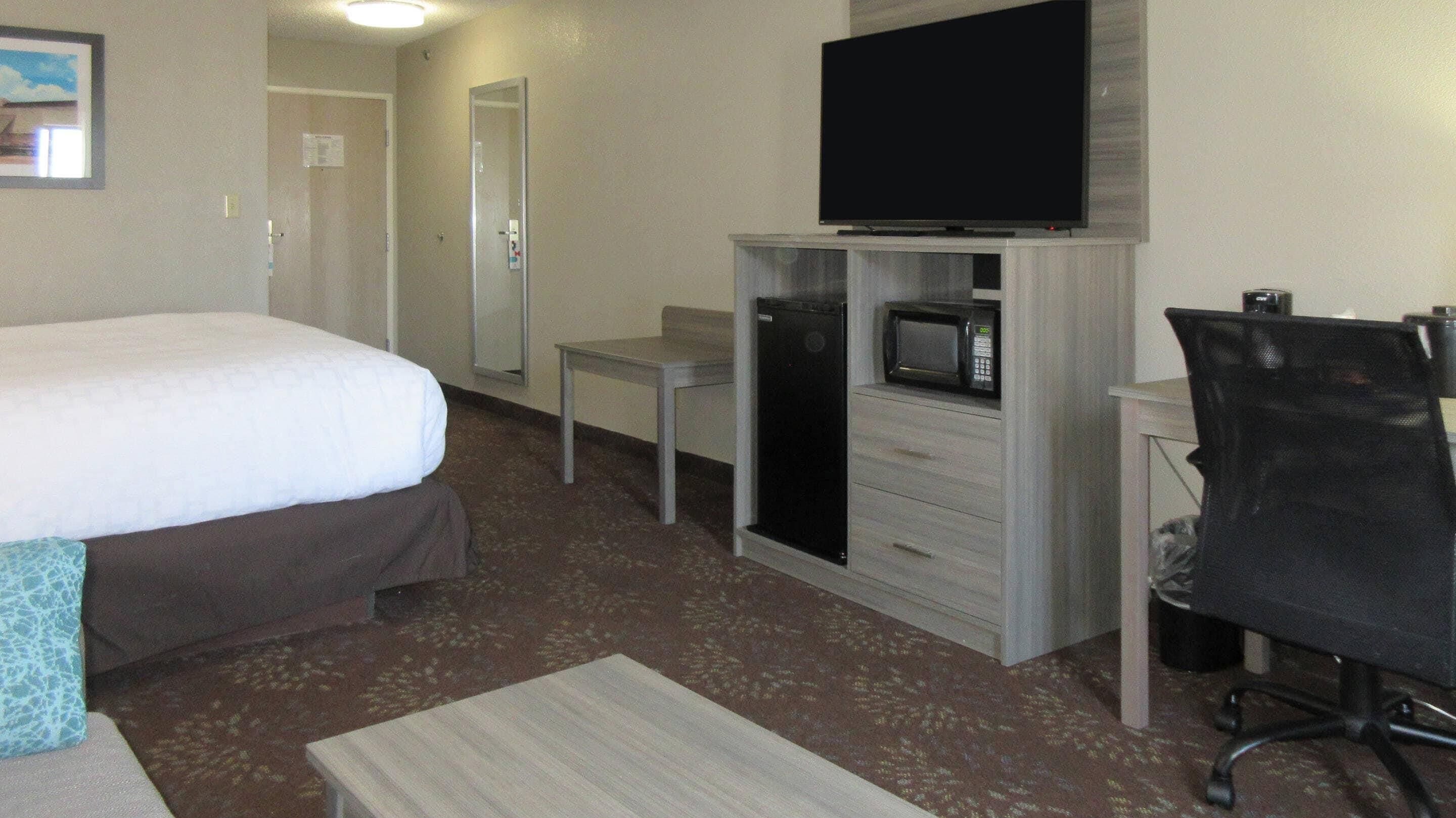 A hotel room with a bed, a desk with a computer, a microwave, a chair, and a television.