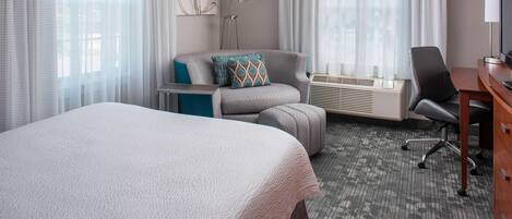 Una habitación de hotel con una cama grande, un escritorio, una silla y una lámpara de pie.
