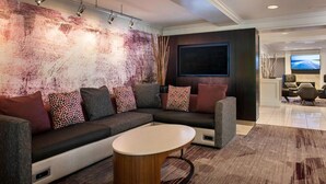 A modern living room with a sectional sofa, a round coffee table, and a large flat-screen TV mounted on the wall. - Sonesta Select Boston Lowell Chelmsford  (Lowell)