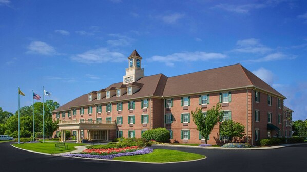 A large brick building with a central tower, multiple windows, and a well-maintained lawn with flower beds. - Sonesta Select Boston Lowell Chelmsford  (Lowell)