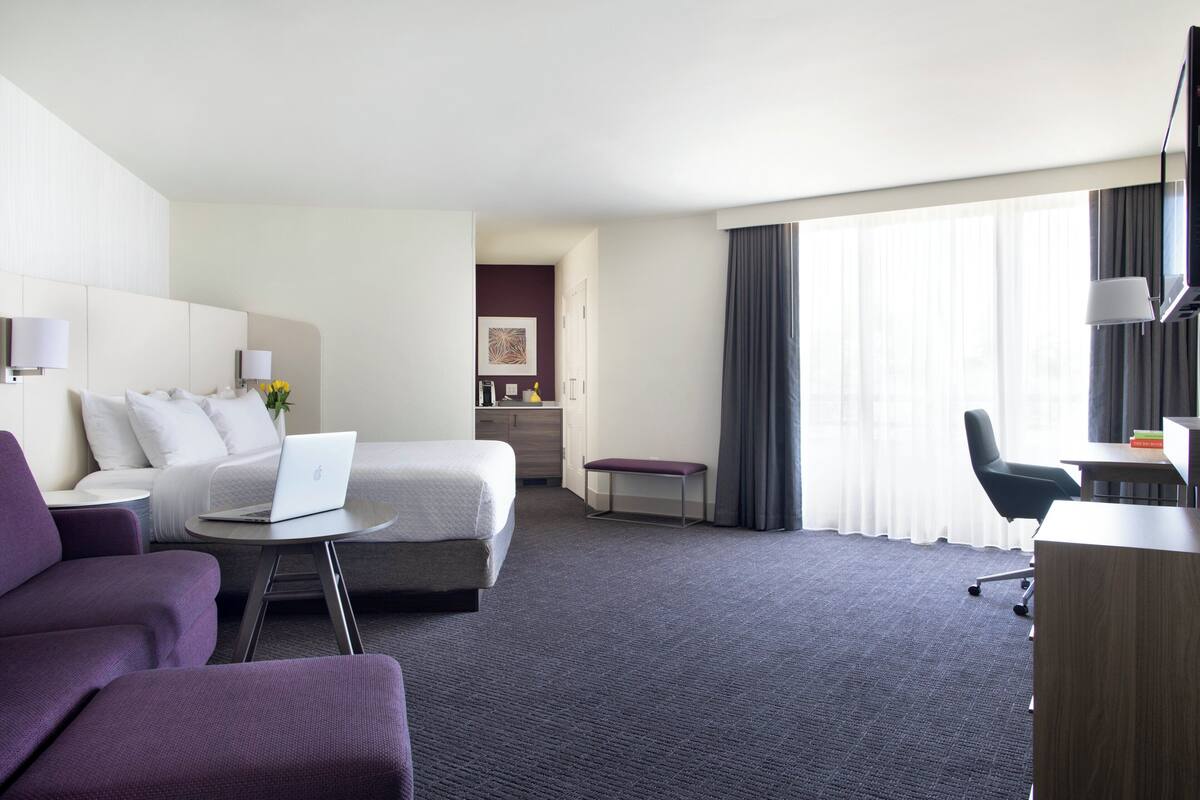 A hotel room with a bed, a desk, a chair, a sofa, and a small table with a laptop.