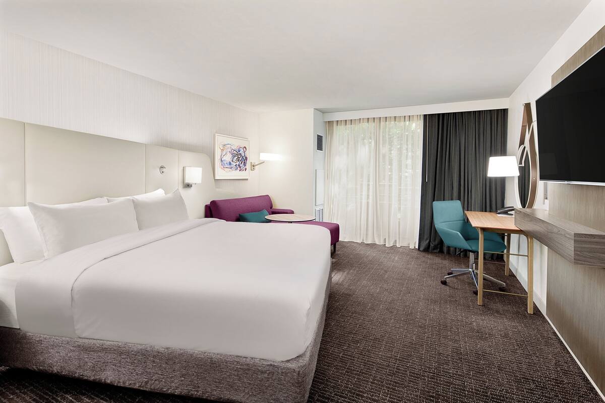 A hotel room with a large bed, a desk, a chair, and a TV.
