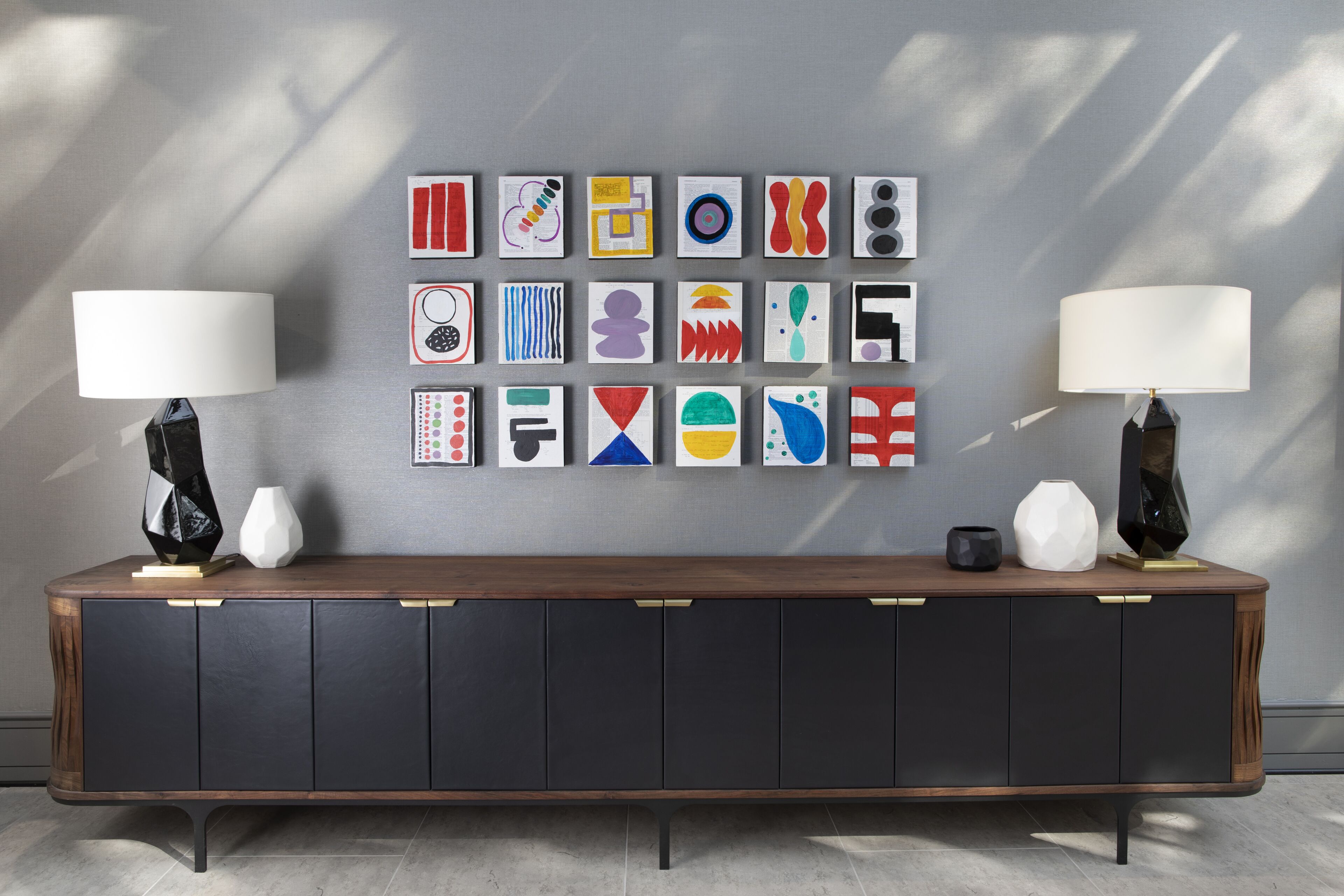 Une pièce moderne avec une console en bois foncé, deux lampes noires et un mur décoré d’œuvres d’art abstraites aux couleurs vives.