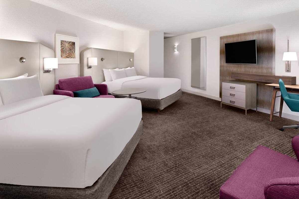 Habitación de hotel con dos camas, un escritorio, una silla, un televisor y una mesita.