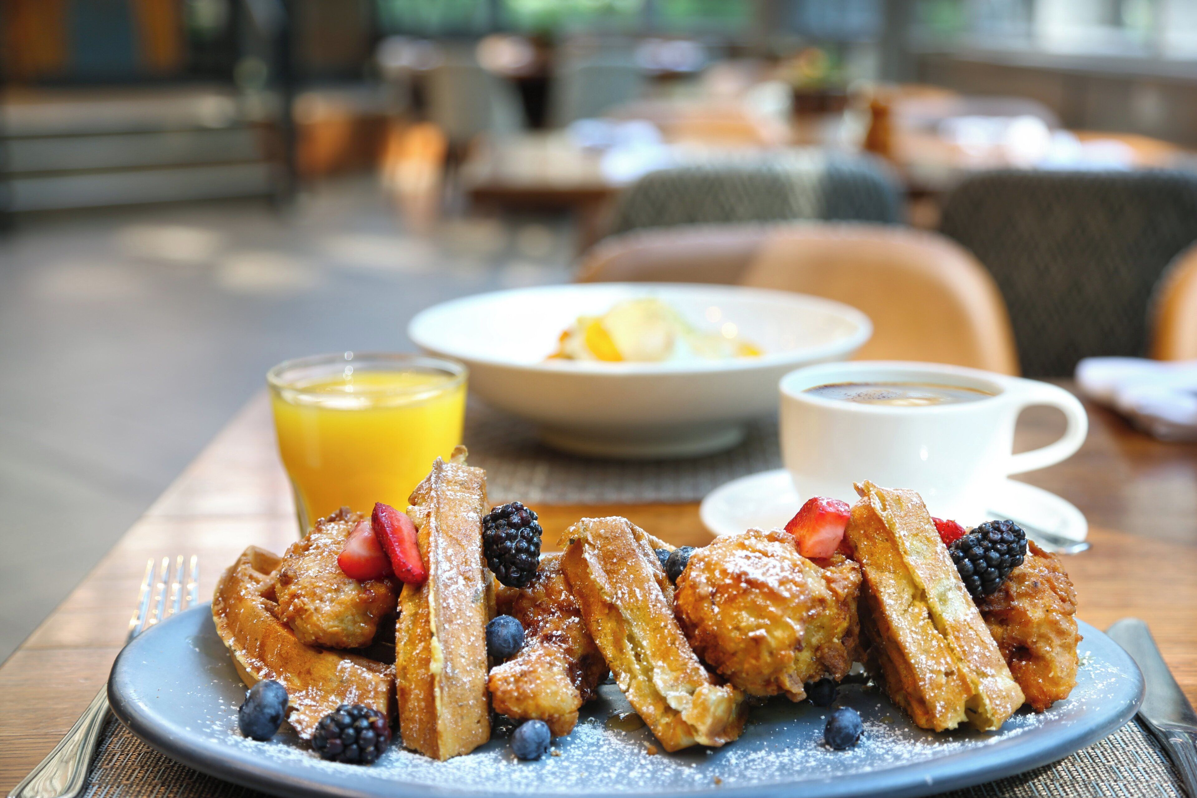 A breakfast plate with waffles, strawberries, blueberries, and blackberries, accompanied by a glass of orange juice and a cup of coffee.