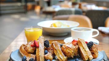 A breakfast plate with waffles, strawberries, blueberries, and blackberries, accompanied by a glass of orange juice and a cup of coffee.