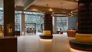 A spacious lobby with a modern design, featuring a reception desk, seating areas, and large windows allowing natural light.