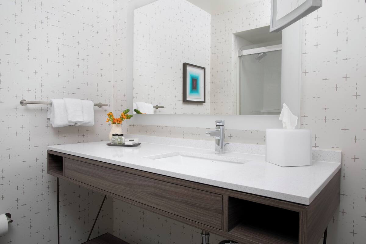 Un baño con lavamanos blanco, espejo y toallero.